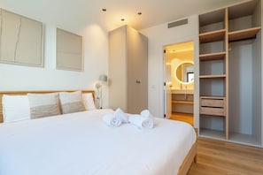 A hotel room with a large bed, a wardrobe, a bathroom with a mirror, and a bedside table with a lamp. - Can Milà Apartments  (Sitges)