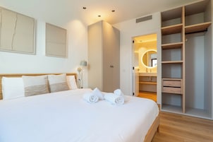 Une chambre d’hôtel avec un grand lit, une armoire, une salle de bain avec un miroir et une table de chevet avec une lampe.