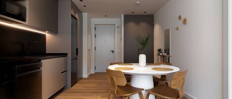 A modern kitchen with built-in appliances, a dining area with a round table and wooden chairs, and a hallway leading to a door.