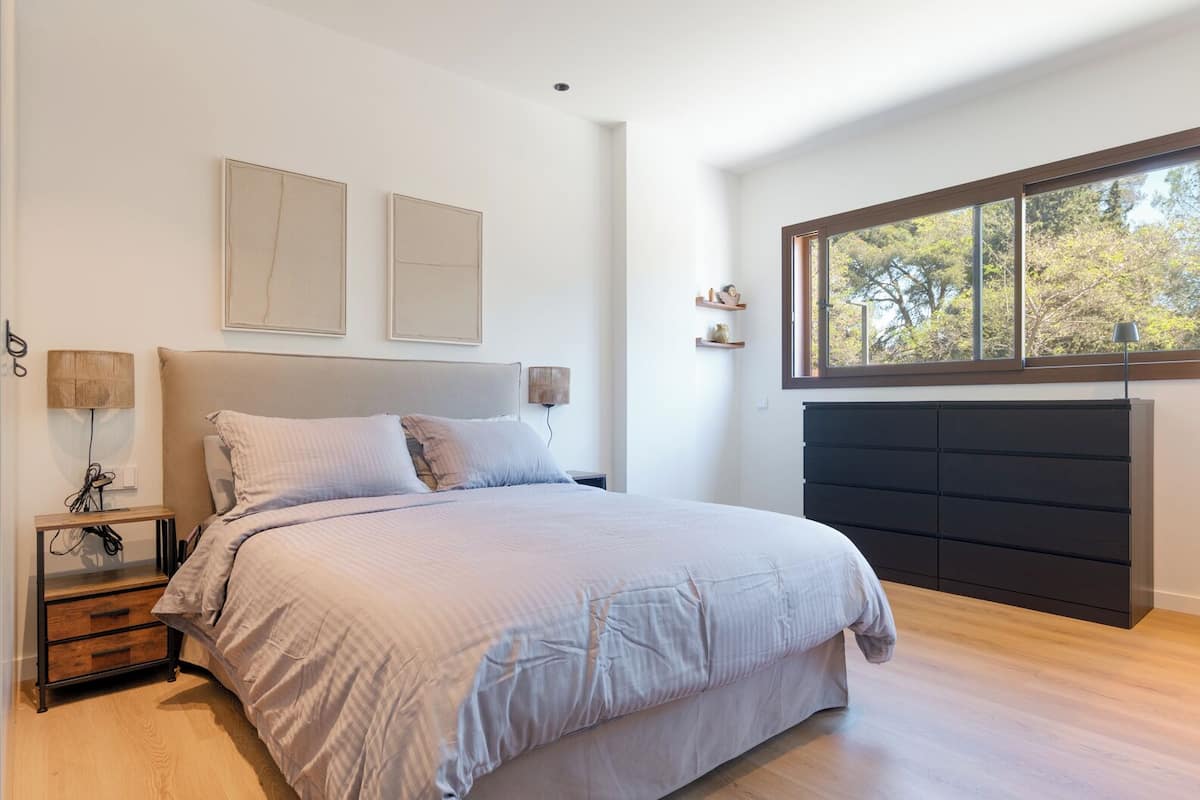 Un dormitorio con cama, mesitas de noche, cómoda y ventana con vista a árboles.
