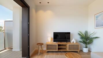 Een moderne woonkamer met een televisie, houten meubels, een plant en uitzicht door een glazen deur.