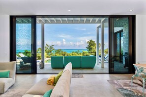 A modern living room with a large sliding glass door leading to an outdoor seating area with a view of the sea.