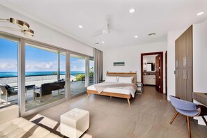 A modern bedroom with a large bed, a seating area, and a view of the beach.