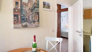 A room with a bed, a white chair, a table with a bottle and glass, and a painting of a street scene on the wall. - Apartment 'Fewo Schwan' with Wi-Fi (Malchow)