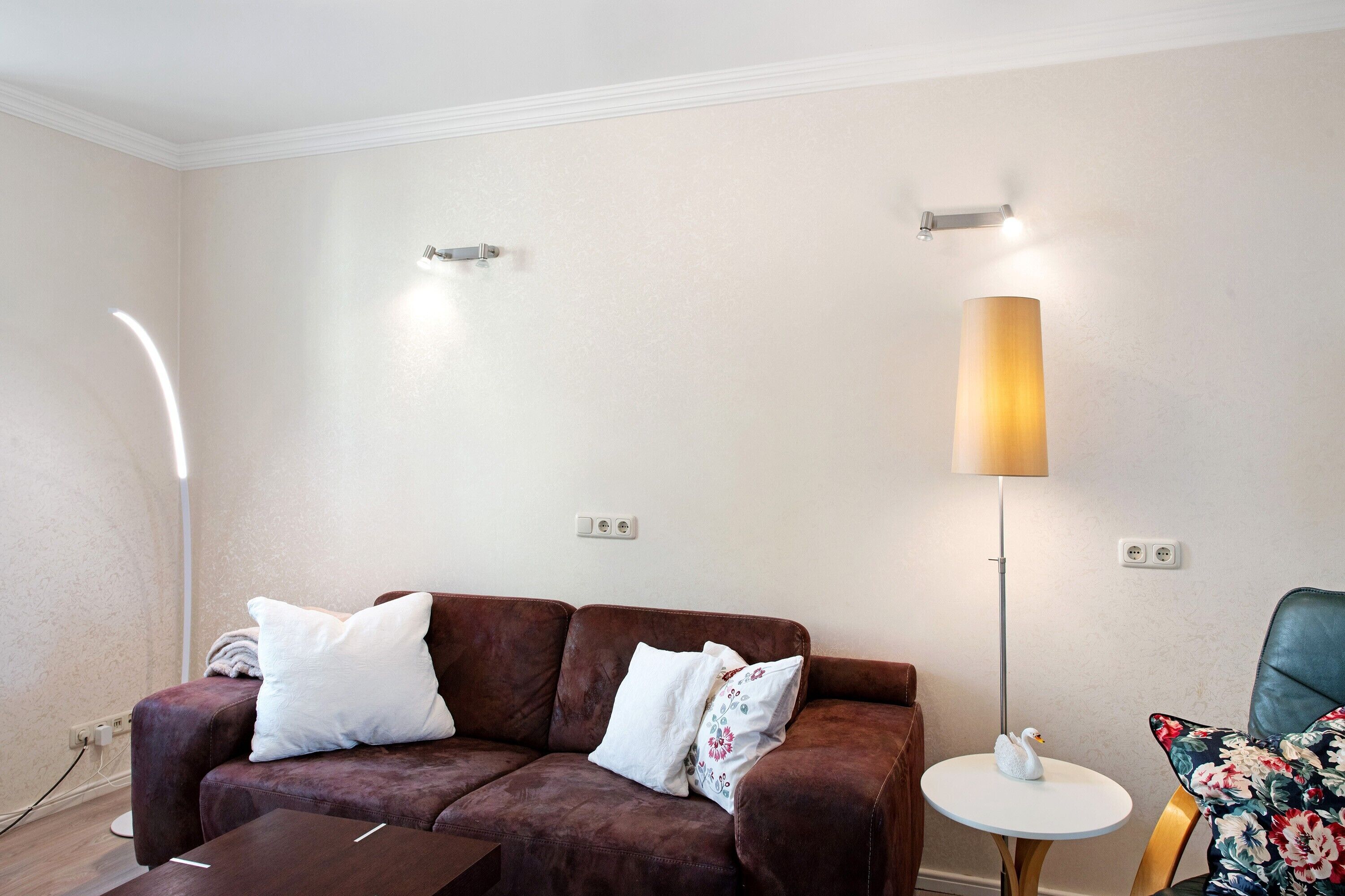 A living room with a brown sofa, white pillows, a small round table with a swan decoration, and a tall floor lamp.