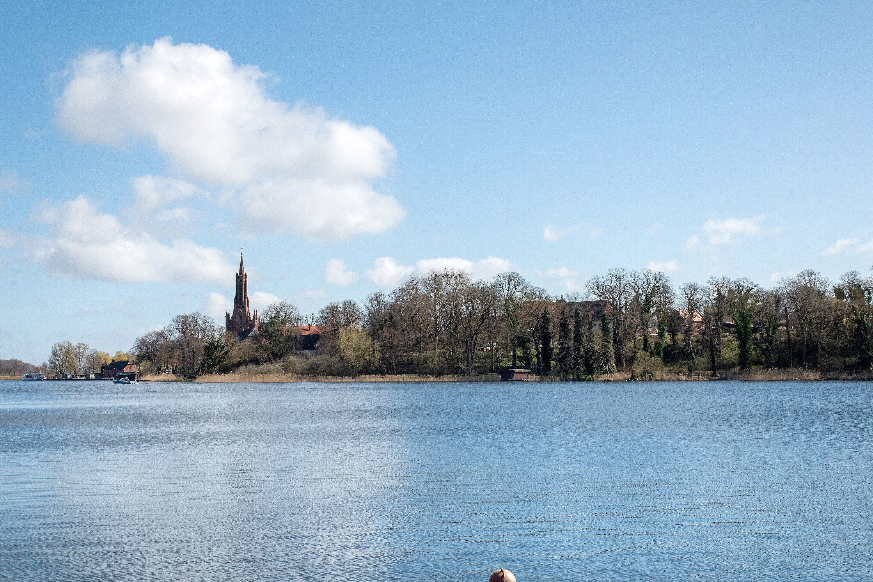 Un lago tranquilo con una iglesia y árboles al fondo.