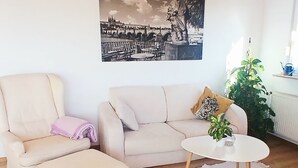 Una sala de estar con sofá, reposapiés y mesa de centro, un cuadro en la pared y una planta.