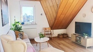 Una sala de estar tipo loft acogedora, con techo inclinado, un sofá, una mesita redonda y un televisor.