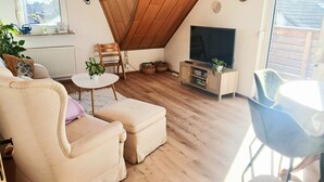 Una sala de estar acogedora con techo inclinado, un televisor, un sofá, una mesita y una silla.