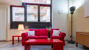 A red sofa with white cushions, a red coffee table, a floor lamp, and a view of balconies through a window. - Loft Vermouth by Wonderful Italy (Torino)