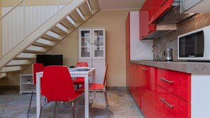 A compact kitchen with red cabinets, a microwave, and a dining area with red chairs and a white table. - Loft Vermouth by Wonderful Italy (Torino)