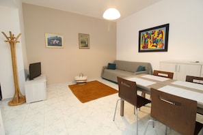 A living room with a sofa, a dining table with chairs, a TV, and a floor lamp. - La Caletta Central-holiday by the sea (La Caletta)