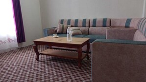 A living room with a checkered carpet, a wooden coffee table, a sofa with striped cushions, and a partially visible armchair. - Annapurna Himdrishya Pokhara Homestay (Pokhara)