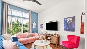 Ein modernes Wohnzimmer mit einem blauen Sofa, einem roten Sessel, einem Fernseher und einer Gitarre an der Wand.