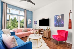 En moderne stue med blå sofa, rød lænestol, fjernsyn og en guitar hængende på væggen.