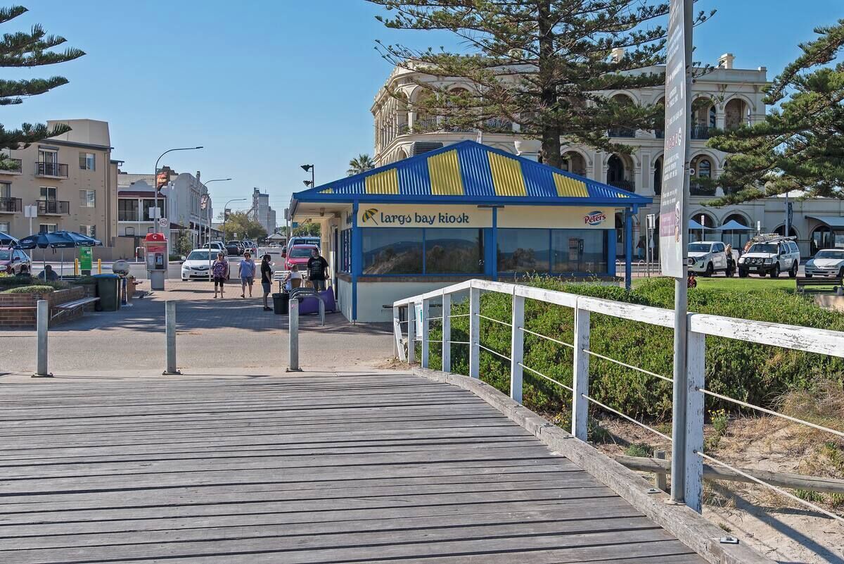 A wooden boardwalk leading to a building with a blue and yellow roof, labeled "Largo's Bay Kiosk."