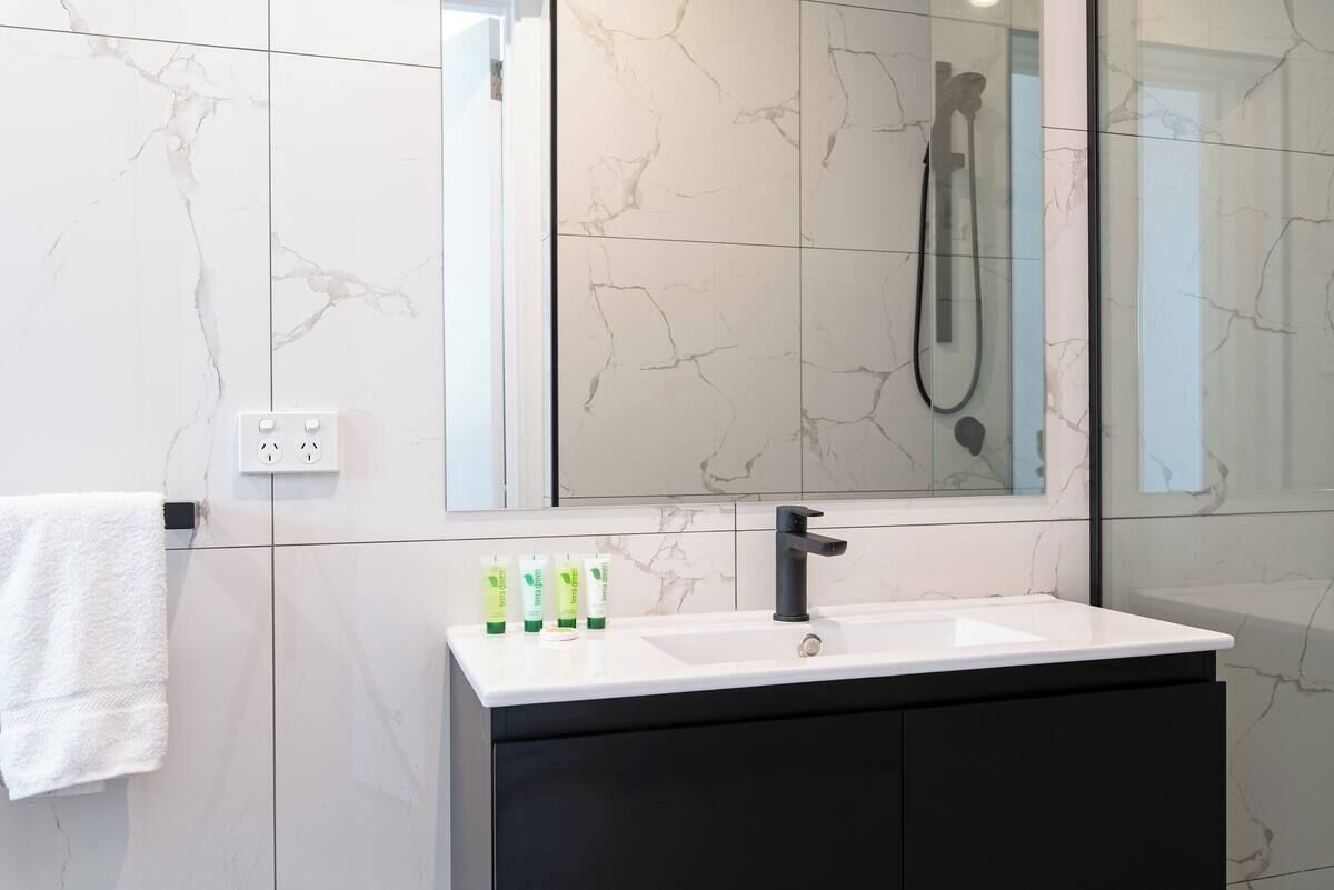 A bathroom with a white sink, black cabinet, and a large mirror reflecting a showerhead.