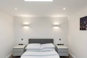 A modern hotel room with a bed, two bedside tables, and a nightstand. - Bright 1 Bedroom Apartment in London (London)