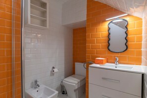 Kylpyhuone, jossa on valkoisia ja oransseja laattoja, pesuallas, peili ja wc-istuin.