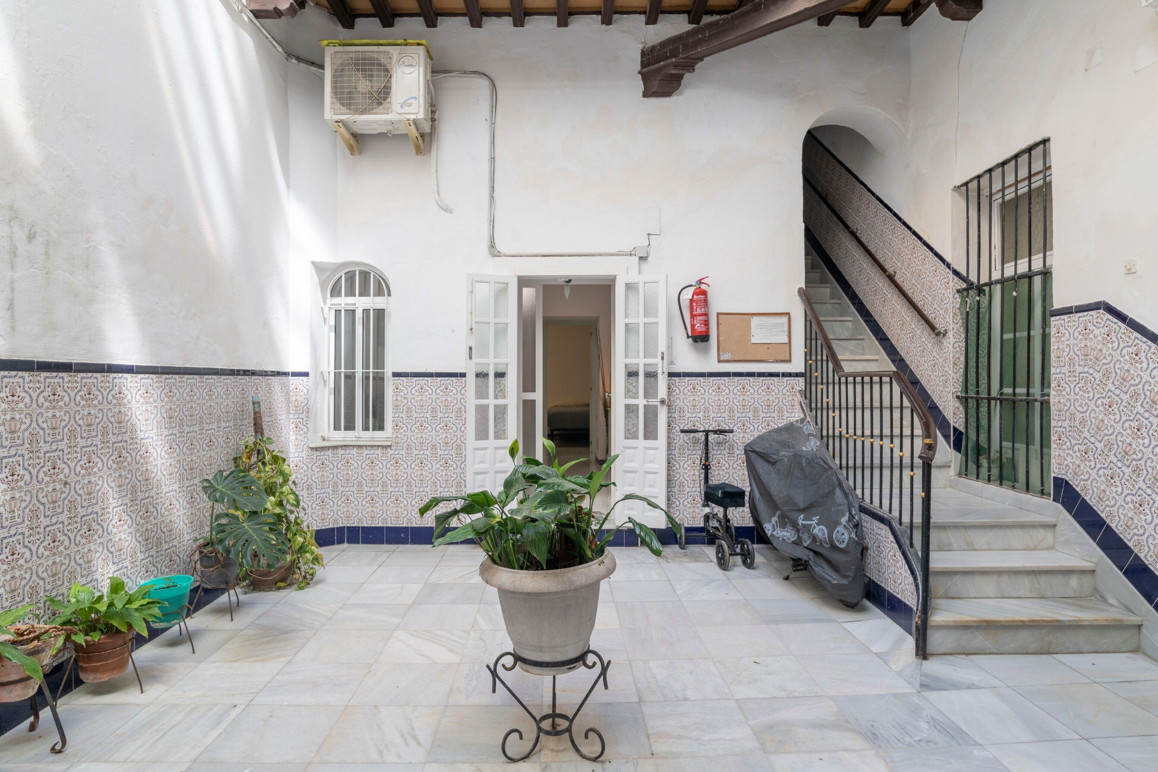 A courtyard with a potted plant, a fire extinguisher, a scooter, and a staircase.