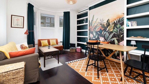 A living room with a sofa, coffee table, and chairs, a bookshelf, and a large painting on the wall. - Chic One-bedroom Apartment in London (London)