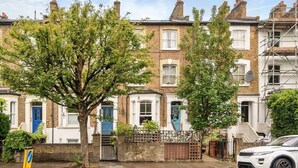 A row of terraced houses with a tree in the foreground, a white car parked on the street, and a yellow sign on the sidewalk. - Chic One-bedroom Apartment in London (London)