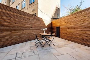 A courtyard with a wooden fence, a table with chairs, and a vase. - Stylish Ground-floor Retreat in Notting Hill (London)