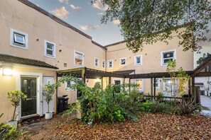 A courtyard with a building featuring multiple windows and a covered area with plants. - Charming 1BR Flat in Sydenham With Free Parking (London)