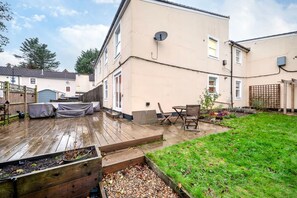 A residential backyard with a wooden deck, a small garden area, and a two-story house. - Charming 1BR Flat in Sydenham With Free Parking (London)