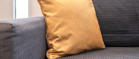 Un sofá gris con un cojín color mostaza.