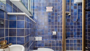 A bathroom with blue tiles, a white sink, a toilet, and a shower area. - Compact Studio in Vibrant Pimlico (London)