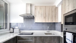 A modern kitchen with grey cabinets, a stainless steel range hood, a built-in oven, and a window providing natural light. - Charming 2-bedroom Apartment in London (London)