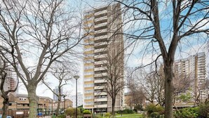A tall residential building with a modern design, surrounded by a well-maintained park with trees and a pathway. - Charming 2-bedroom Apartment in London (London)