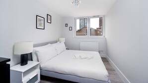 A bedroom with a bed, nightstands, a window, and framed pictures on the wall. - Charming 2-bedroom Apartment in London (London)