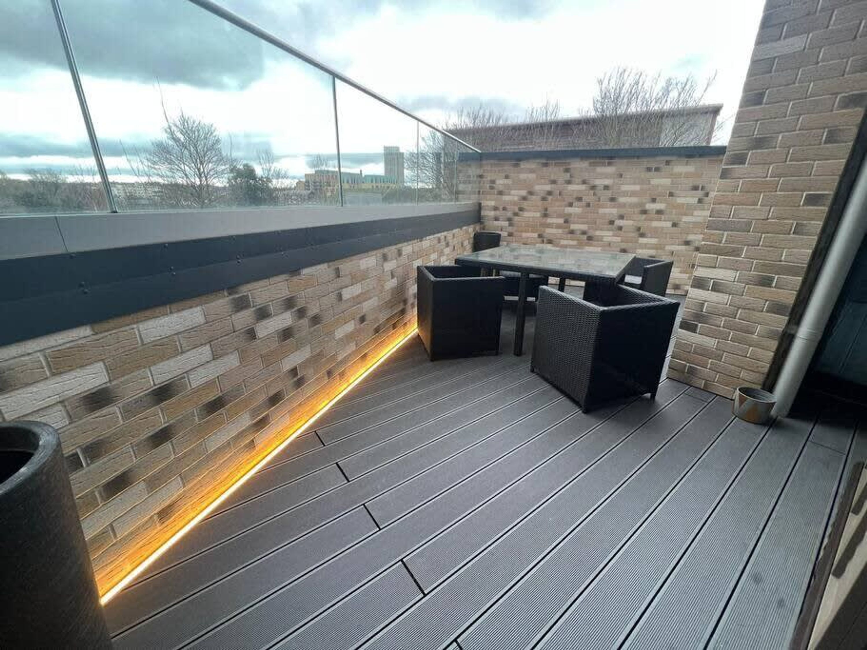 An outdoor patio with a brick wall, a table with chairs, and a low wall with a light strip.