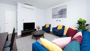 Ein modernes Wohnzimmer mit einer Couch, zwei Sesseln, einem Couchtisch, einem Fernseher und einer Pflanze.