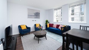 Ein modernes Wohnzimmer mit einer Couch, zwei Sesseln, einem Couchtisch, einem Fernseher und einem Esstisch.