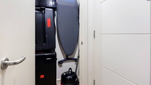 Een kleine kamer met een bed, een verwarming, een strijkplank en een waterkoker.