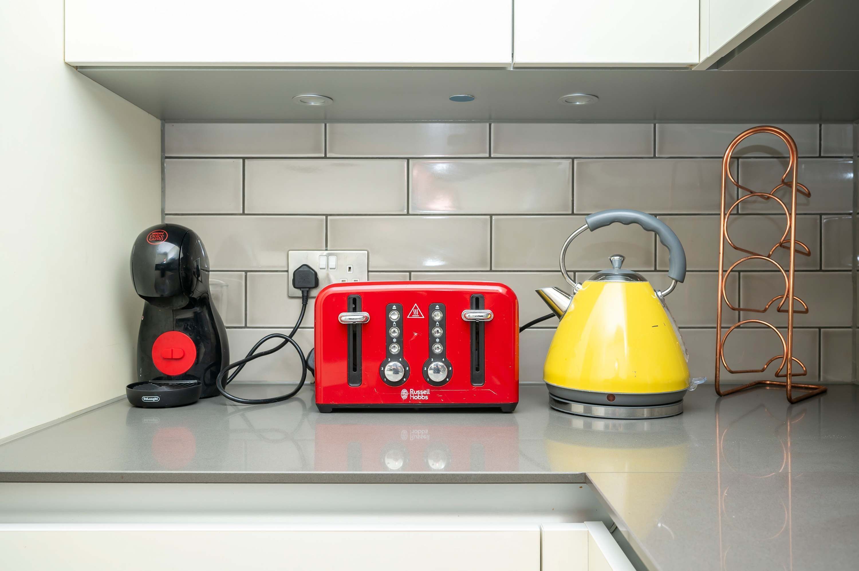 A kitchen counter with a red toaster, a yellow kettle, and a black coffee maker.