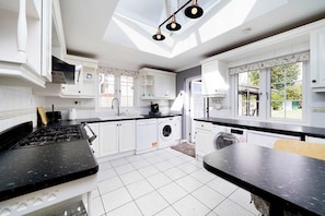 Cozinha moderna com armários brancos, bancada preta, máquina de lavar embutida e claraboia.