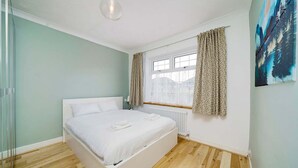 Ein Schlafzimmer mit einem Einzelbett, einem Fenster mit Vorhängen, einem Heizkörper und einem Bild an der Wand.