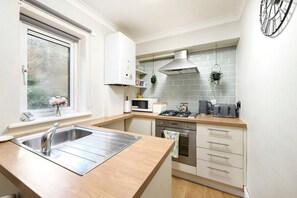A compact kitchen with a sink, stove, microwave, and cabinets. - Cozy One-bedroom Flat in Slough (Slough)