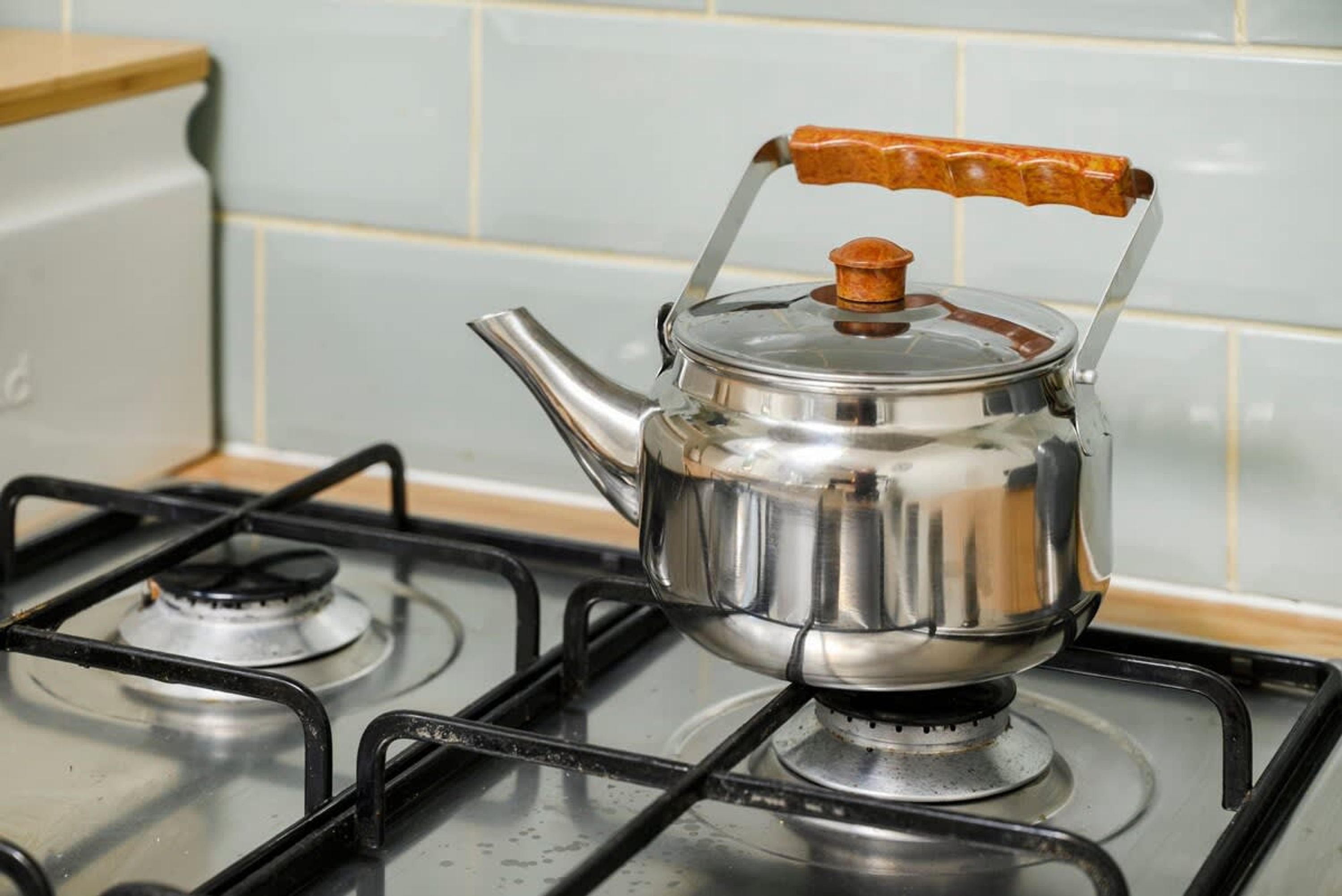A stainless steel kettle with a wooden handle on a gas stove.