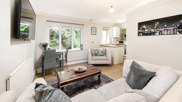 A modern living room with a sofa, coffee table, and a dining area with a chair and table. - Cozy One-bedroom Flat in Slough (Slough)