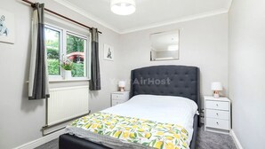 A bedroom with a bed, a window with curtains, a bedside table with a lamp, and a radiator. - Cozy One-bedroom Flat in Slough (Slough)