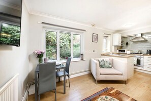 A modern kitchen with white cabinets, a built-in oven, and a large window overlooking greenery. - Cozy One-bedroom Flat in Slough (Slough)