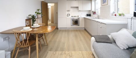 A modern kitchen with white cabinets, a wooden dining table, and a sofa with cushions.