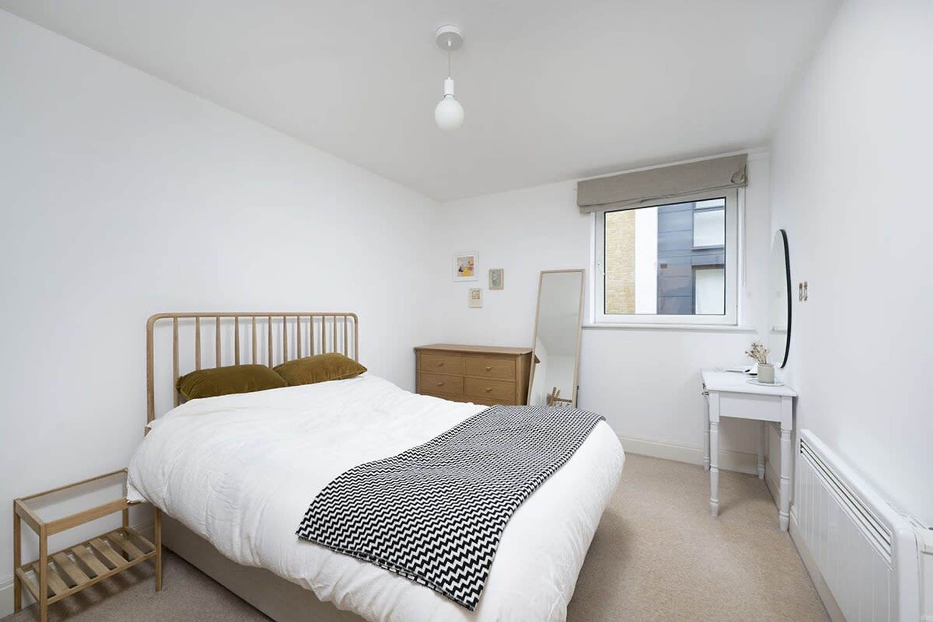 A bedroom with a bed, bedside table, dresser, and a window.