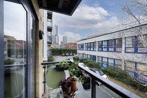 Ein Balkon mit Blumentöpfen, einem Stuhl und Blick auf eine Stadtansicht mit Gebäuden und einem Parkplatz.