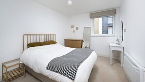 Quarto com cama, mesa de cabeceira, cômoda e janela.